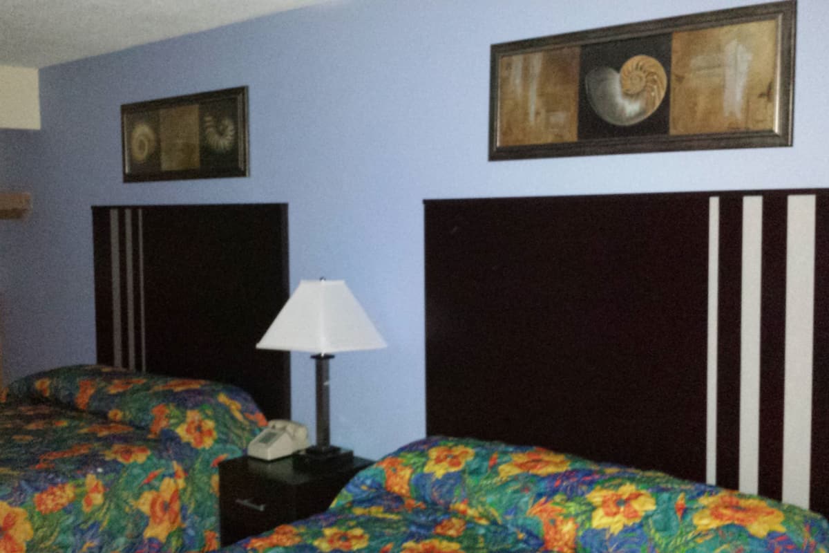 A bedroom with two beds, a nightstand, a lamp, and a framed picture on the wall.