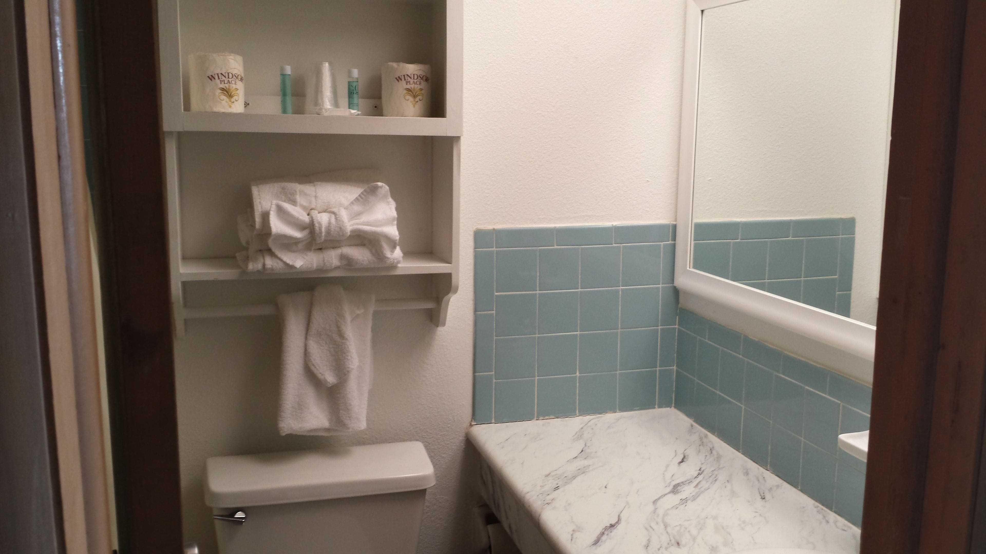 Un baño con inodoro, lavamanos con encimera de mármol, toallero con toalla y estantes con artículos de aseo.