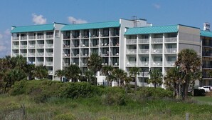 A multi-story hotel with balconies, surrounded by palm trees and greenery. - Bermuda Sands on the Boardwalk (Myrtle Beach)