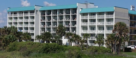 A multi-story hotel with balconies, surrounded by palm trees and greenery.