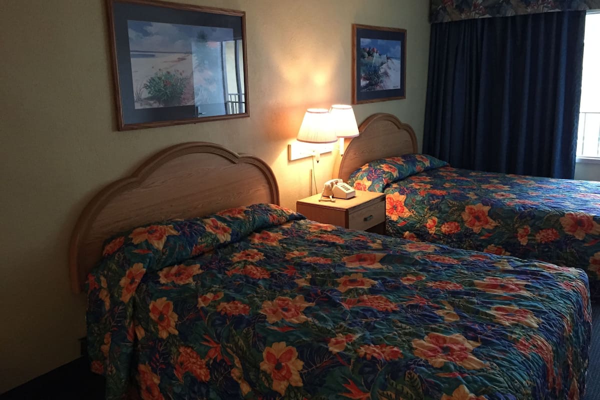 A hotel room with two beds, each with floral bedding, a bedside lamp, and a telephone.