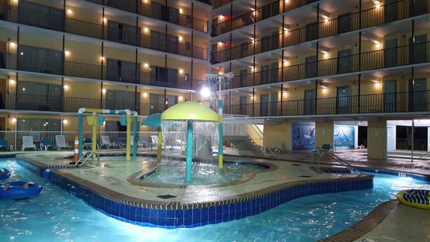 An indoor swimming pool with multiple levels of balconies, lounge chairs, and a water feature. - Bermuda Sands on the Boardwalk (Myrtle Beach)