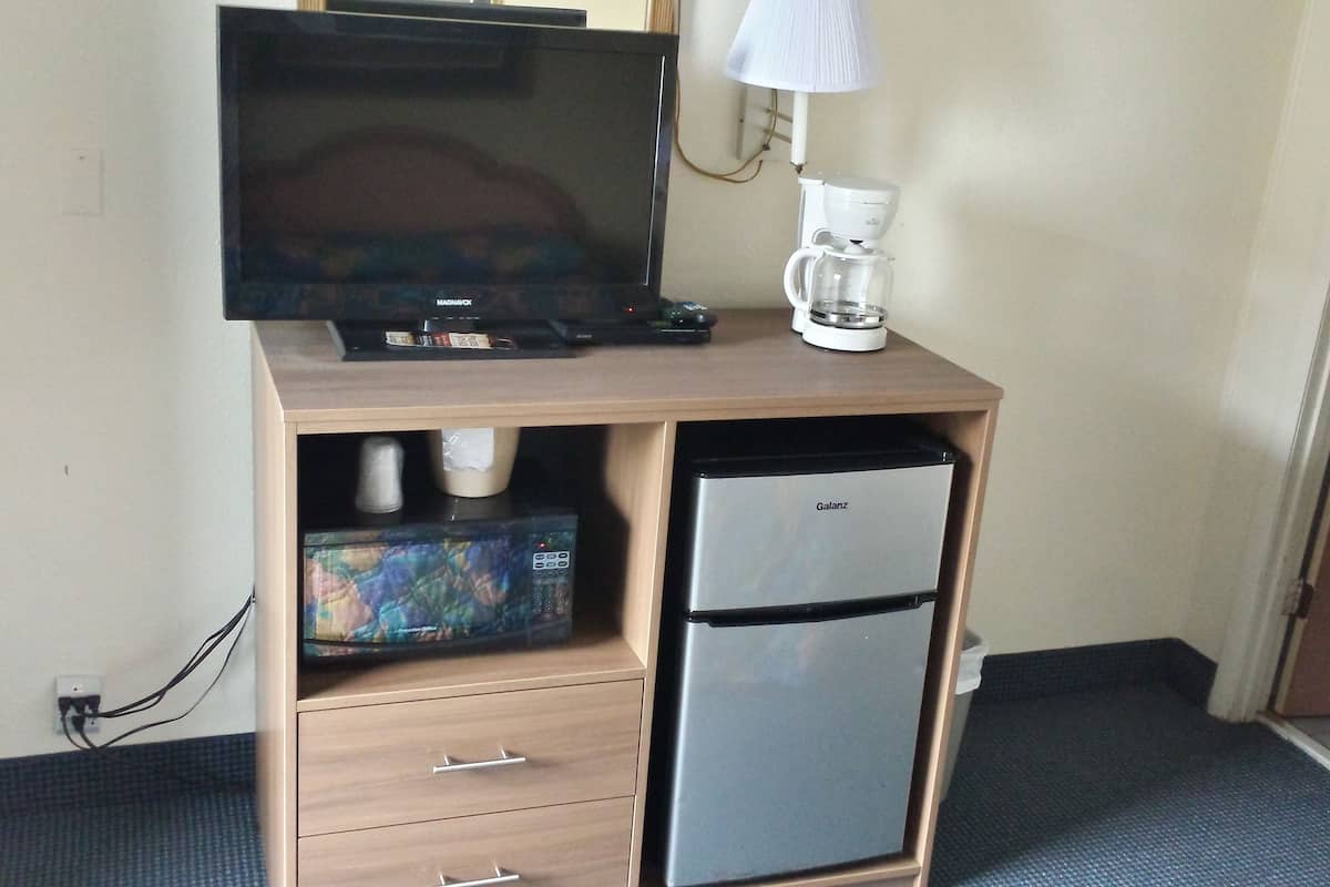 A compact hotel room with a wooden desk, a flat-screen TV, a coffee maker, and a refrigerator.