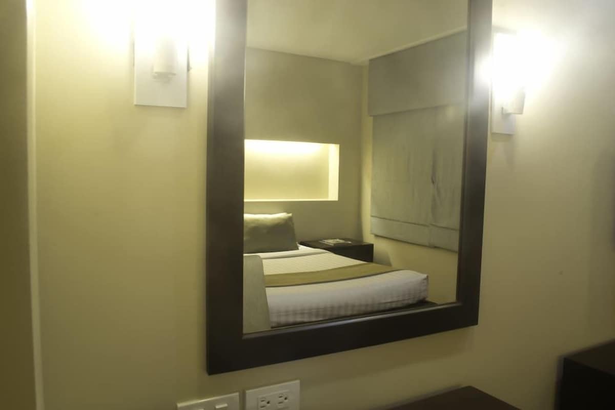 A hotel room with a large mirror, a bed with a white bedspread, and a nightstand with a lamp.