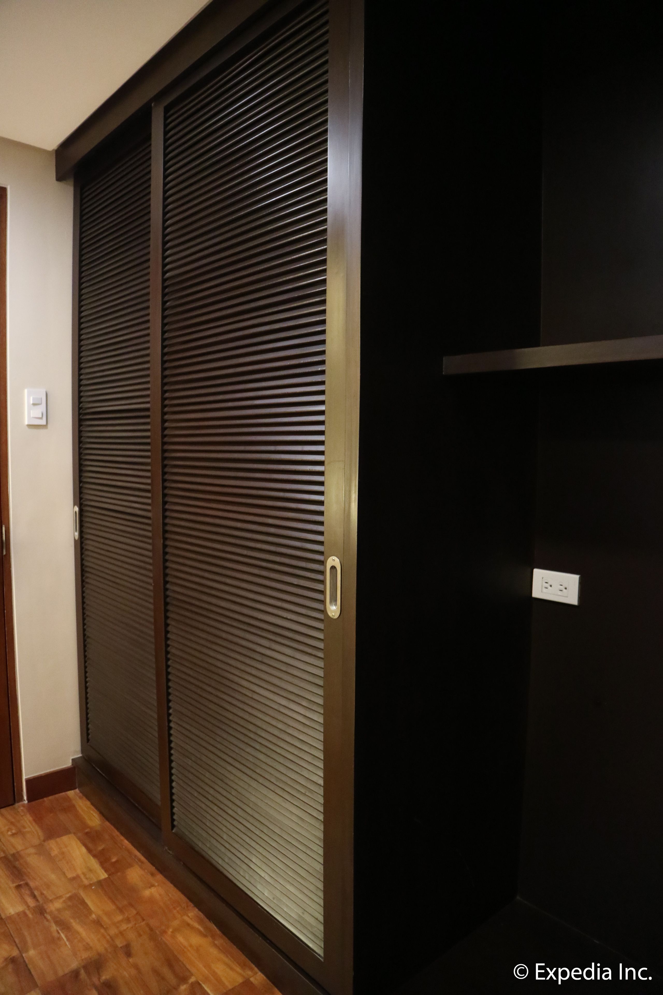 A hallway with a wooden floor and a sliding door with horizontal blinds.