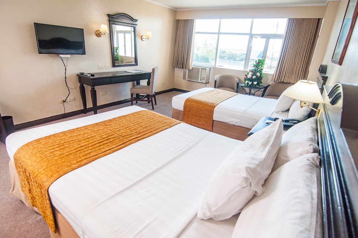 A hotel room with two beds, a desk, a television, and a window with curtains.
