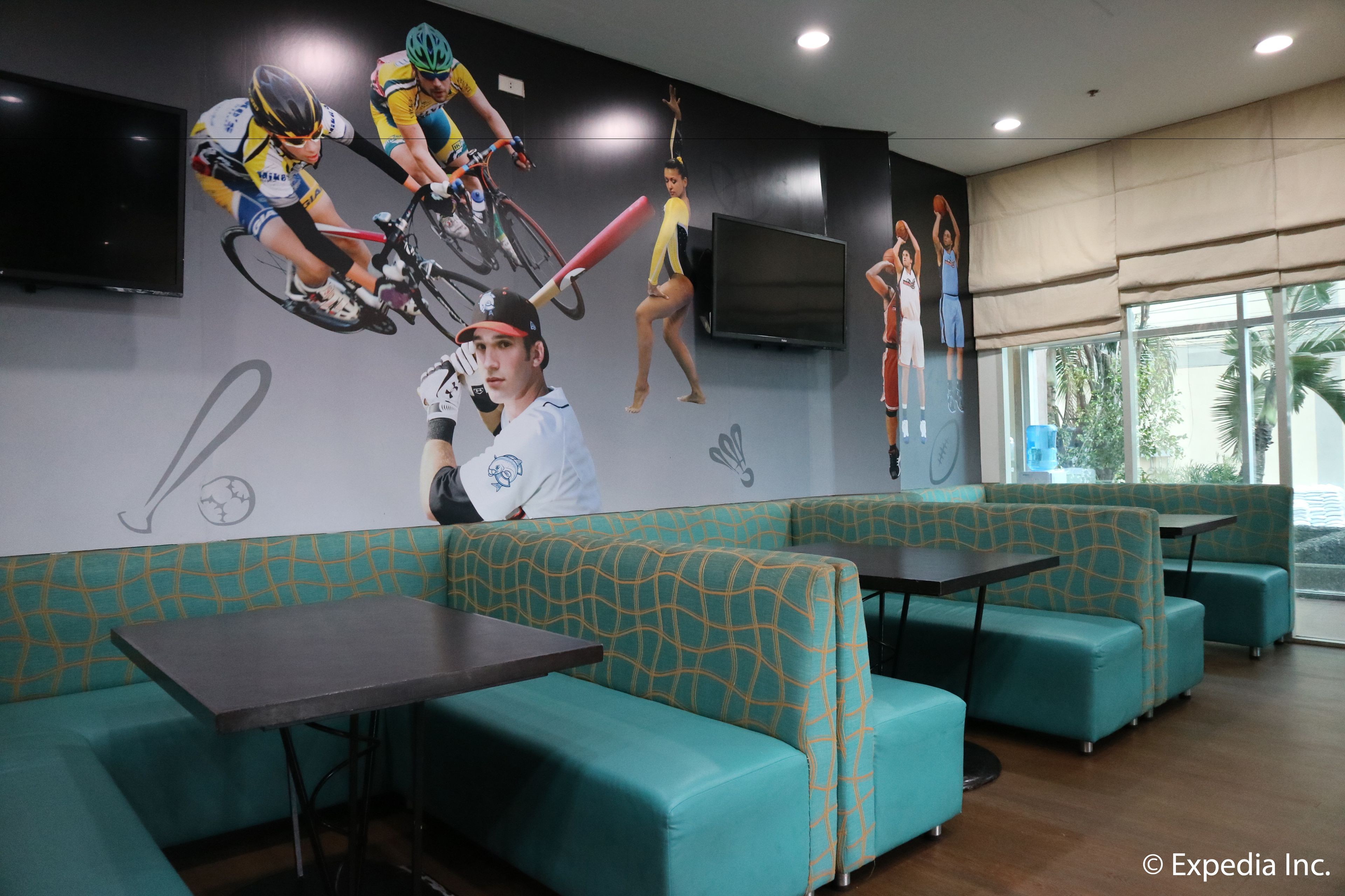 A restaurant with teal cushioned booths, a flat-screen TV, and sports-themed wall art.