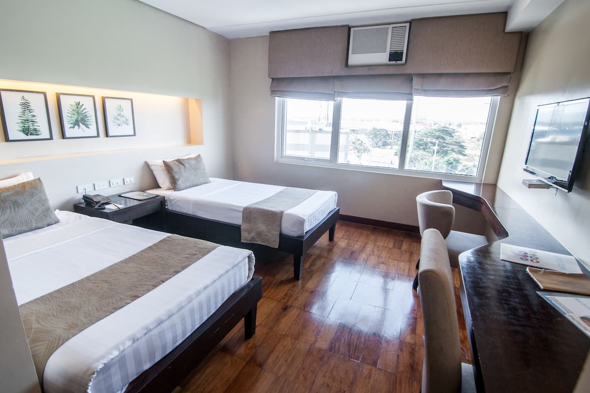 A hotel room with two beds, a desk, a chair, a TV, and a window with a city view.