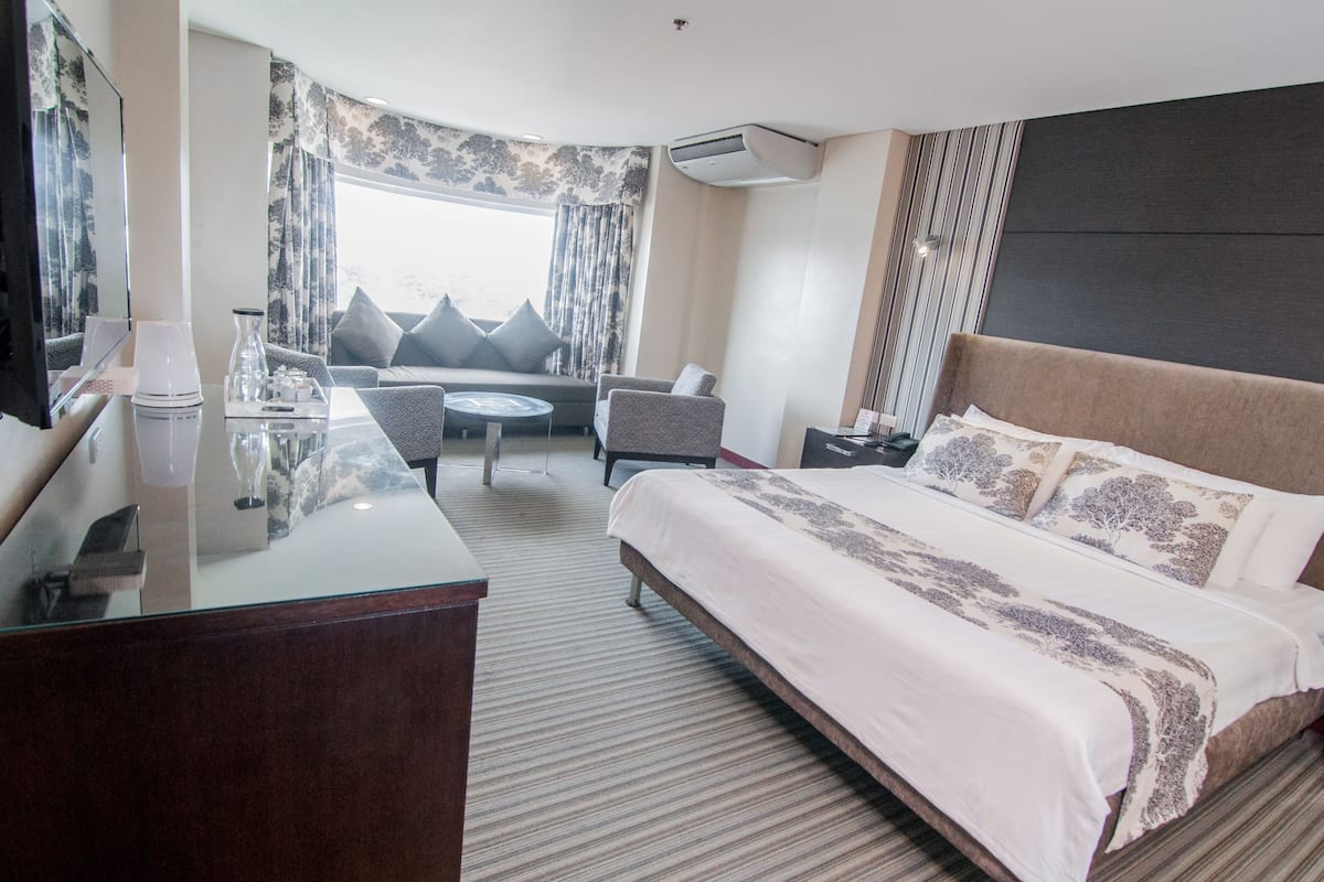 A hotel room with a large bed, a desk, a chair, a small table, and a sofa.
