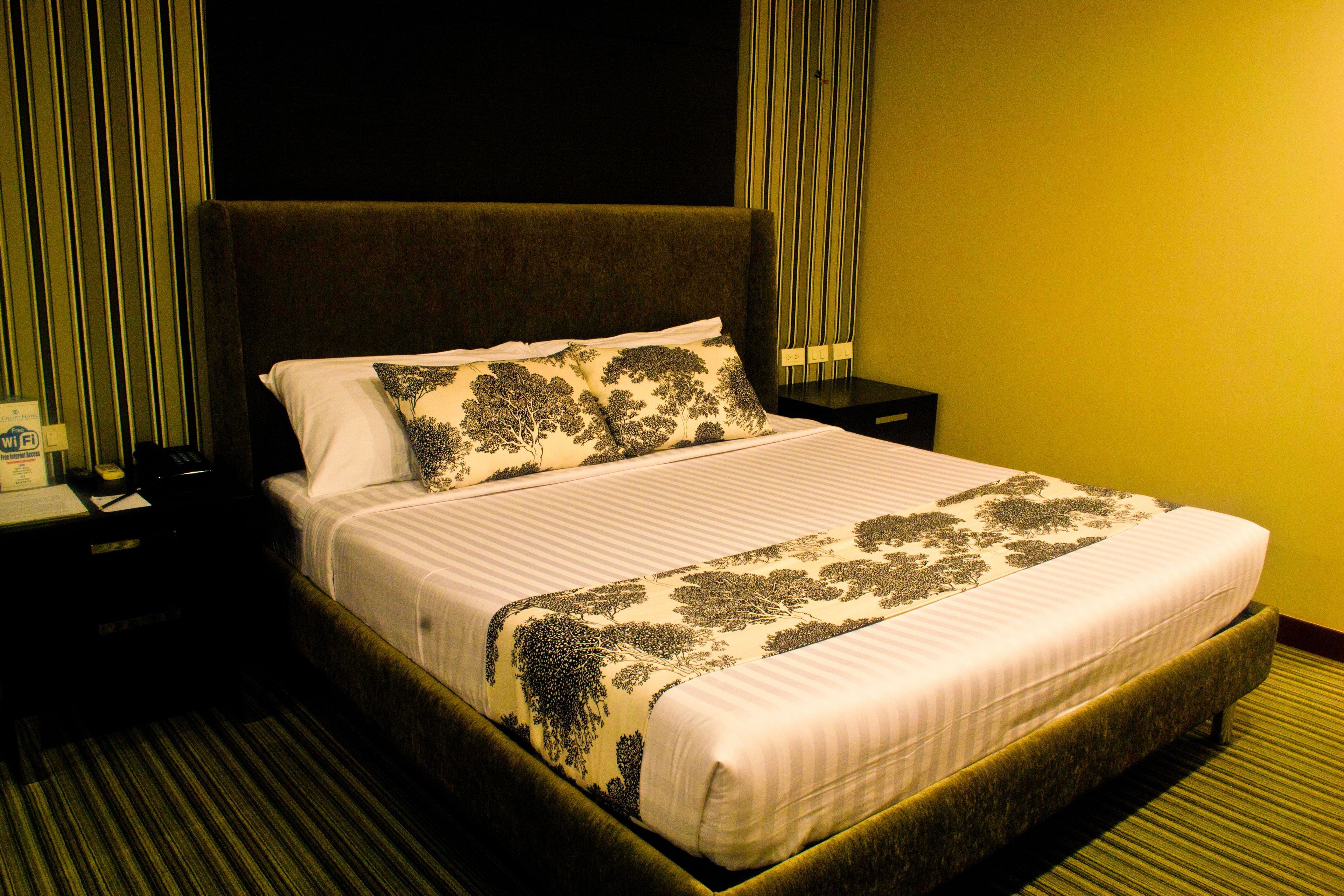 A hotel room with a large bed, a nightstand, and a lamp.