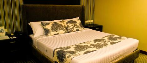 A hotel room with a large bed, a nightstand, and a lamp.