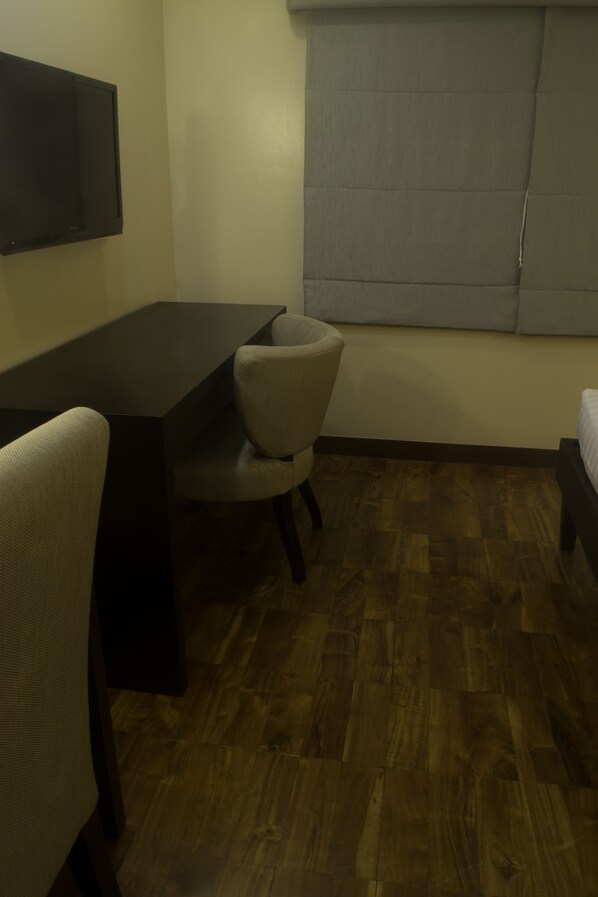 A room with a wooden floor, a bed, a desk, and a chair.