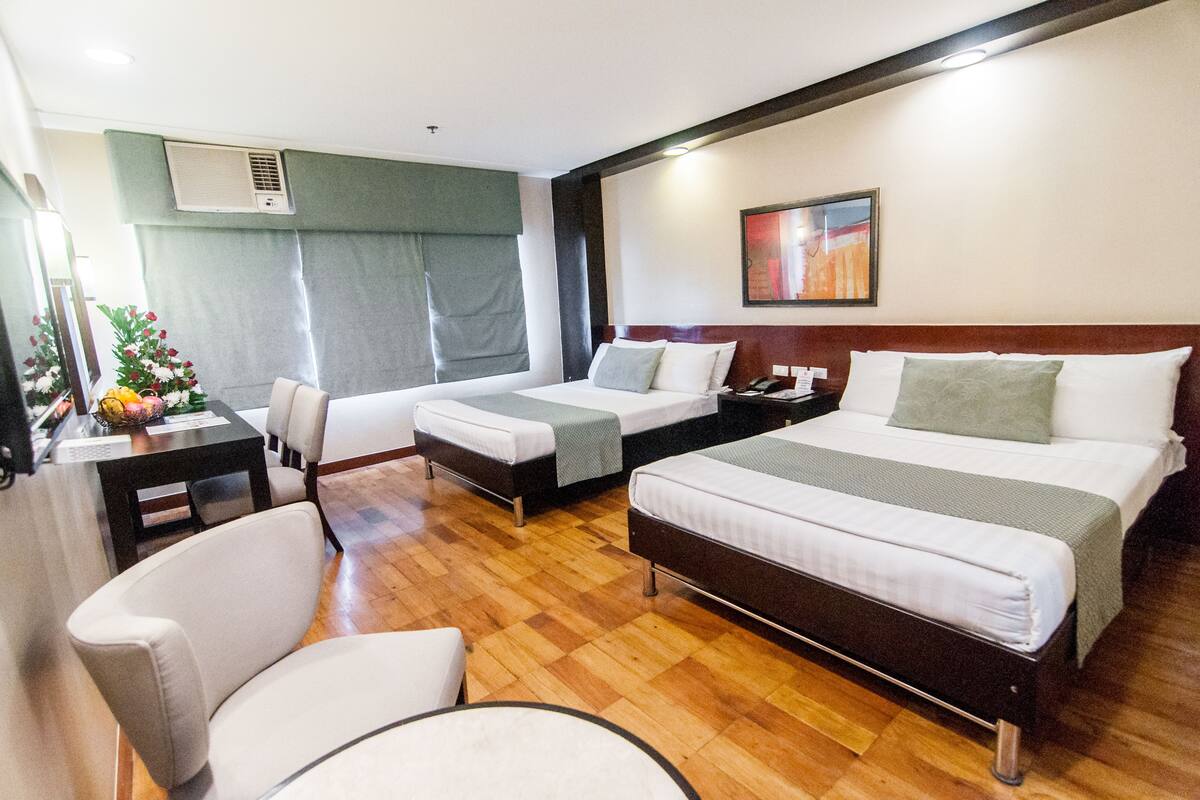 A hotel room with two single beds, a double bed, a desk with a chair, and a small table with a vase of flowers.