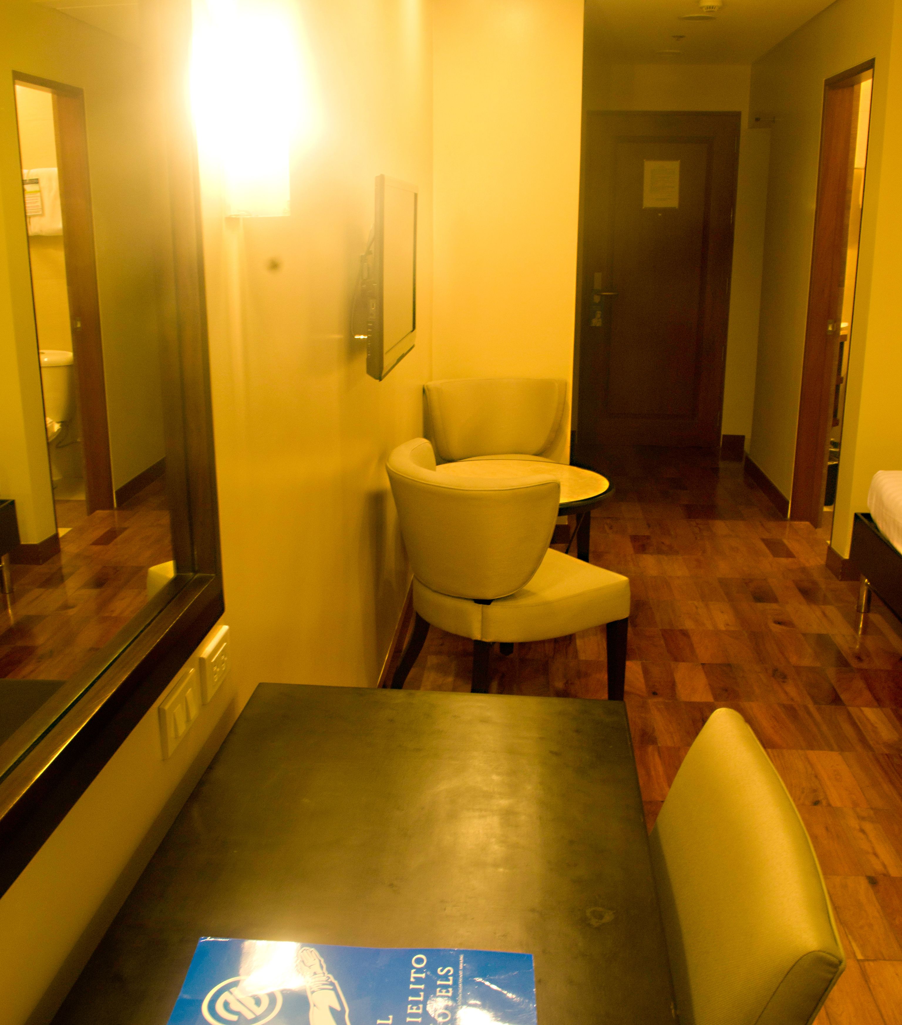 A hotel room with a dining table, a chair, a mirror, and a door in the background.