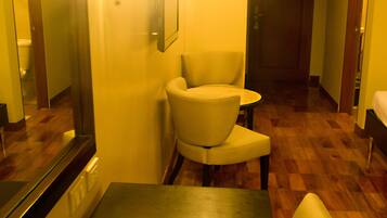 A hotel room with a dining table, a chair, a mirror, and a door in the background.