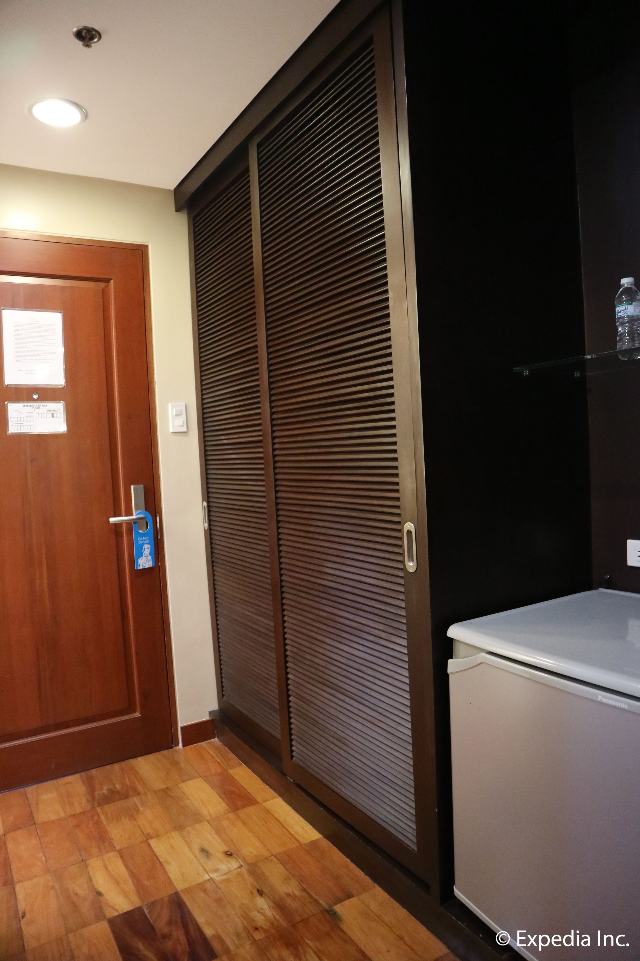 Una habitación con puerta de madera, un armario corredero con asa de metal y un refrigerador blanco.