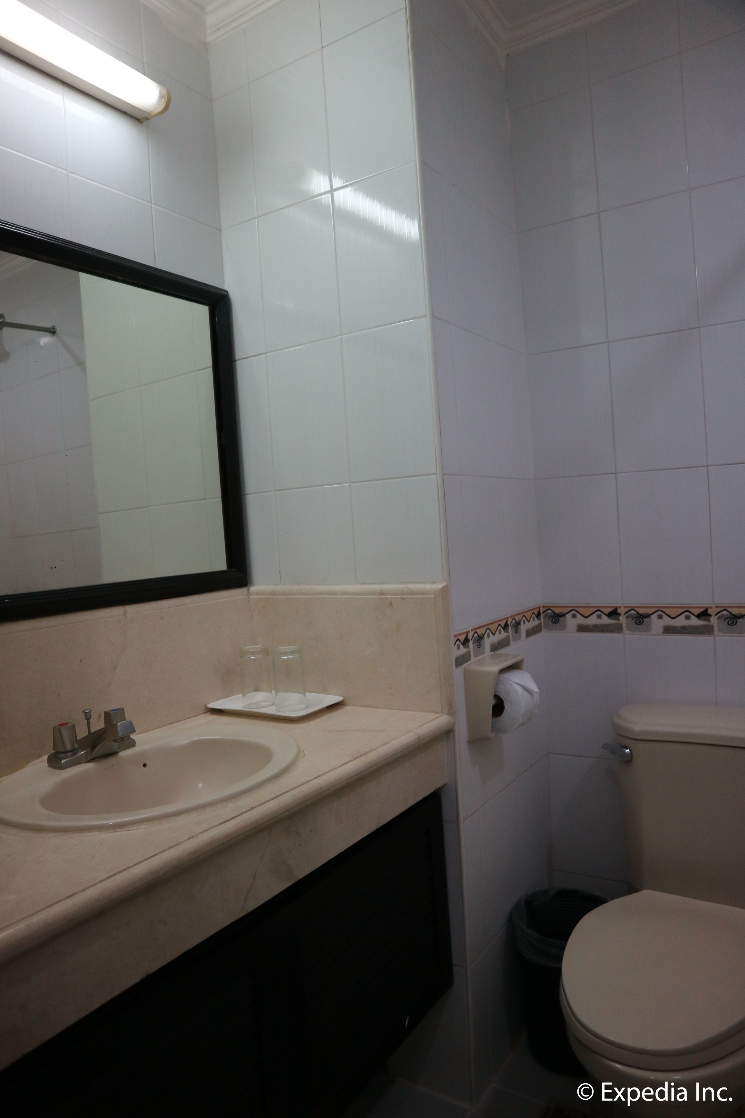 A bathroom with a sink, mirror, toilet, and trash can.