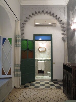 Un baño con piso a cuadros, una puerta verde, un espejo y un perchero.