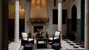 A lobby with a fireplace, two armchairs, a small table, and patterned floor tiles. - Riad Arous Chamel (Tangier)