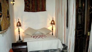 A room with a bed, two bedside lamps, a patterned rug, and a small table with a vase. - Riad Arous Chamel (Tangier)