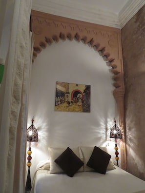 Quarto com uma cama, duas luminárias na parede e um quadro sobre a cama.