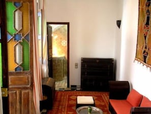 Una habitación con una puerta de madera, un sofá rojo, un tapete estampado y un armario.