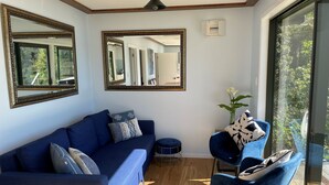 A modern living room with a blue sofa, two armchairs, and a coffee table. There are two large mirrors on the walls and a small side table with a vase of flowers. - The Lodge At Te Rawa - Boat Access Only (Te Rawa)