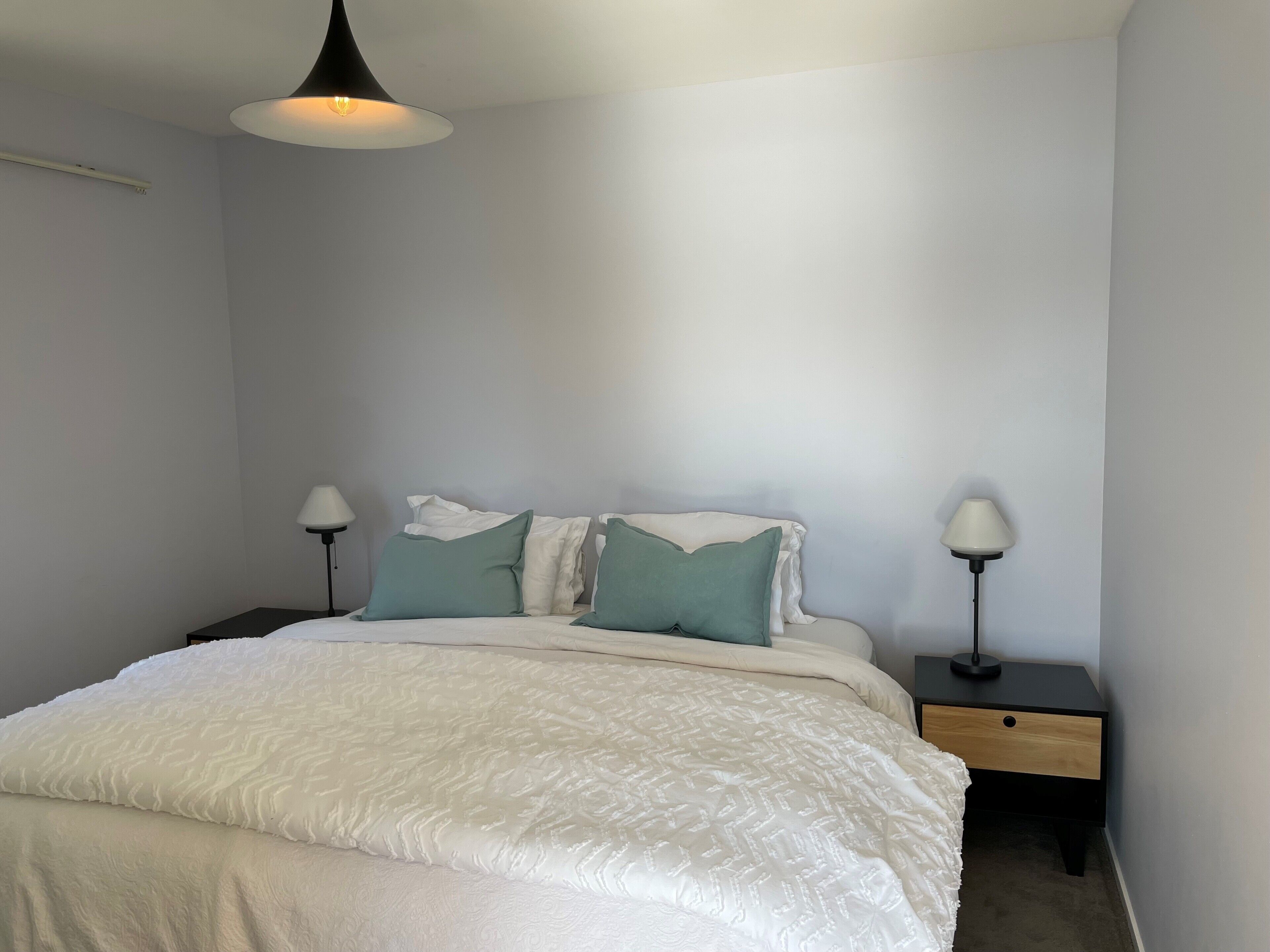 A bedroom with a bed, two bedside tables, and a hanging light fixture.