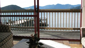 A balcony with a wooden railing, a view of a lake, and mountains in the background. - The Lodge At Te Rawa - Boat Access Only (Te Rawa)