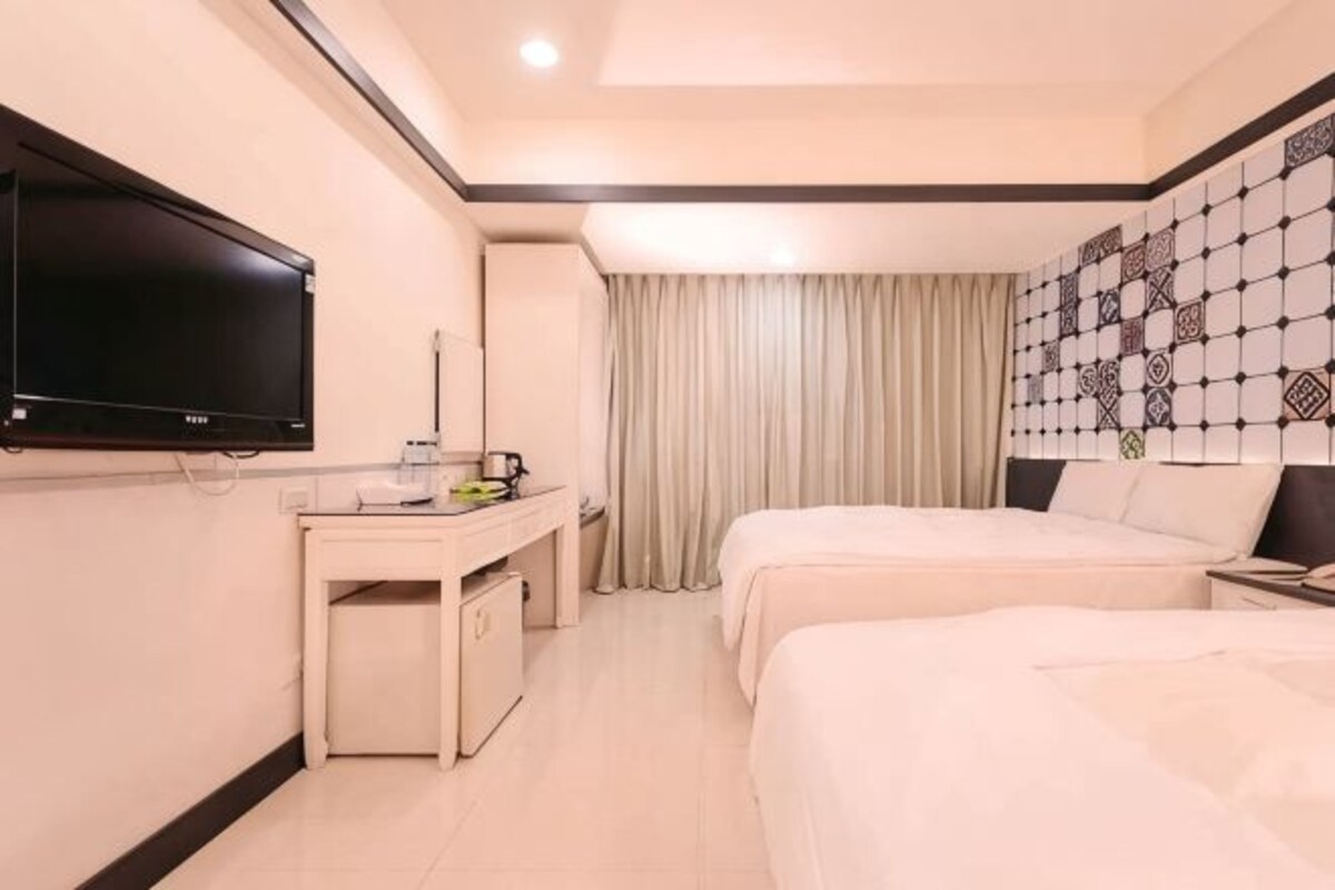 A hotel room with a bed, a desk, a TV, and a patterned wall.