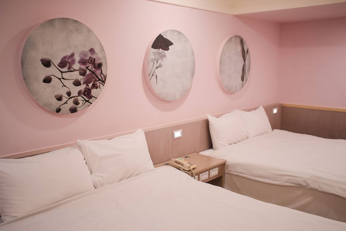 A hotel room with two beds, a nightstand with a telephone, and three wall-mounted artworks.