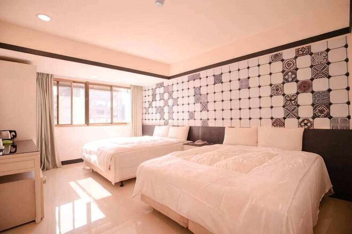 A hotel room with two beds, a desk, and a patterned wall.