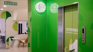 A hotel lobby with green walls, a reception desk, a seating area, and an elevator with a digital display. - Kiwi Express Hotel - Taichung Station Branch 10 (Taichung)