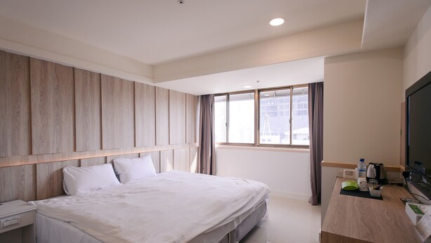 A hotel room with a large bed, a wooden headboard, a desk with a television, and a window with curtains. - Kiwi Express Hotel - Taichung Station Branch 10 (Taichung)