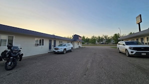 A motel with a parking lot, a motorcycle, and two SUVs parked in front. - Shannon Motel (Fort Nelson)
