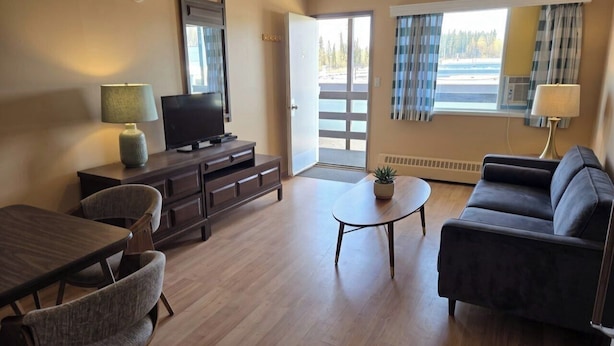 A room with a TV, sofa, dining table, chairs, and a small table with a plant. - Shannon Motel (Fort Nelson)