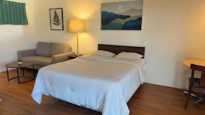 A hotel room with a large bed, a sofa, a small table, a lamp, and a painting on the wall. - Shannon Motel (Fort Nelson)