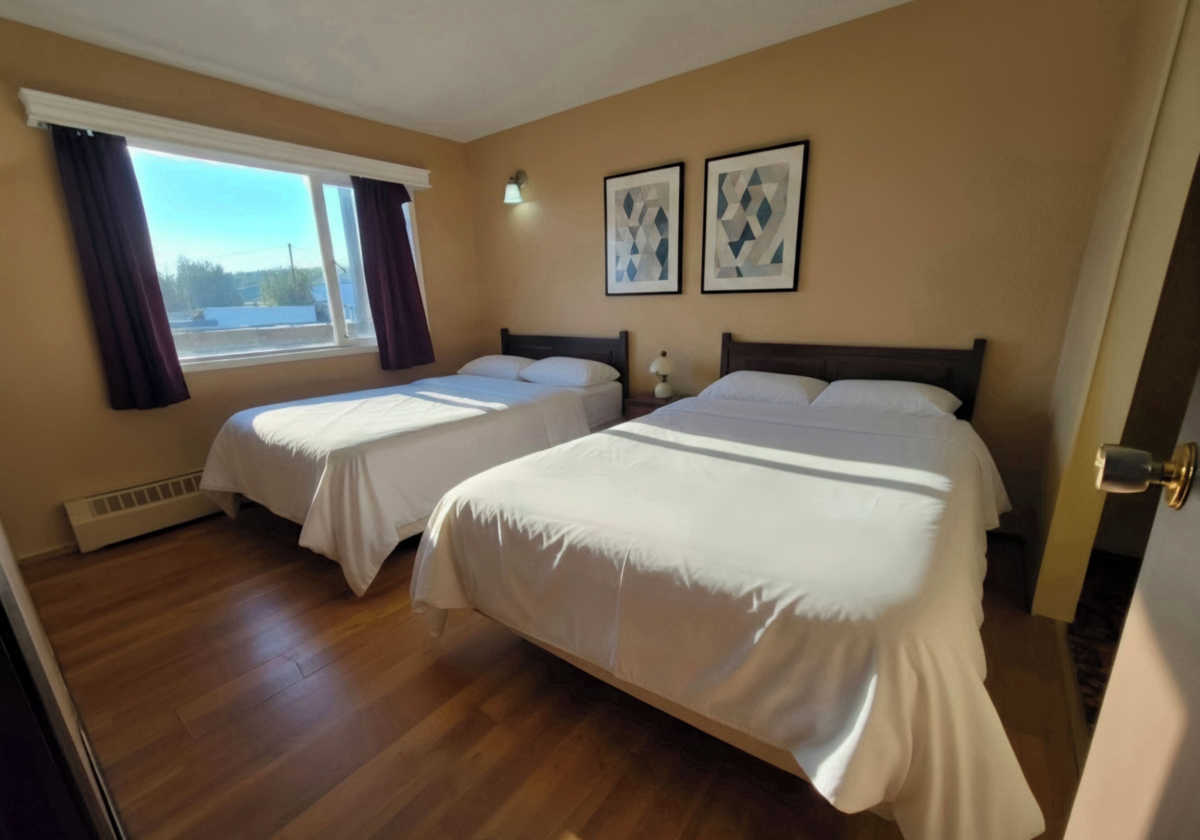 A hotel room with two beds, a window with curtains, and two framed pictures on the wall.