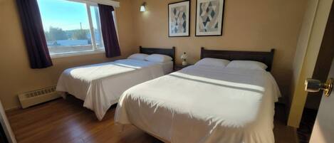 A hotel room with two beds, a window with curtains, and two framed pictures on the wall.
