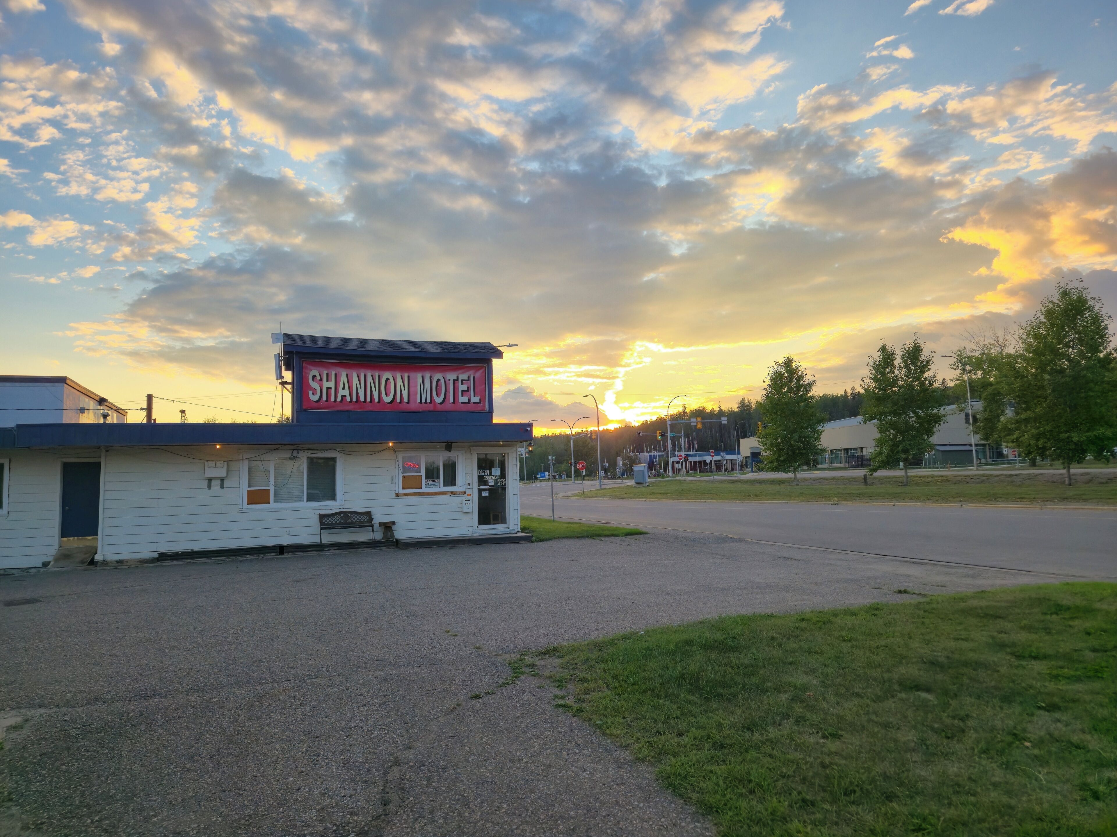 Un motel con un letrero llamativo, un estacionamiento y un atardecer de fondo.