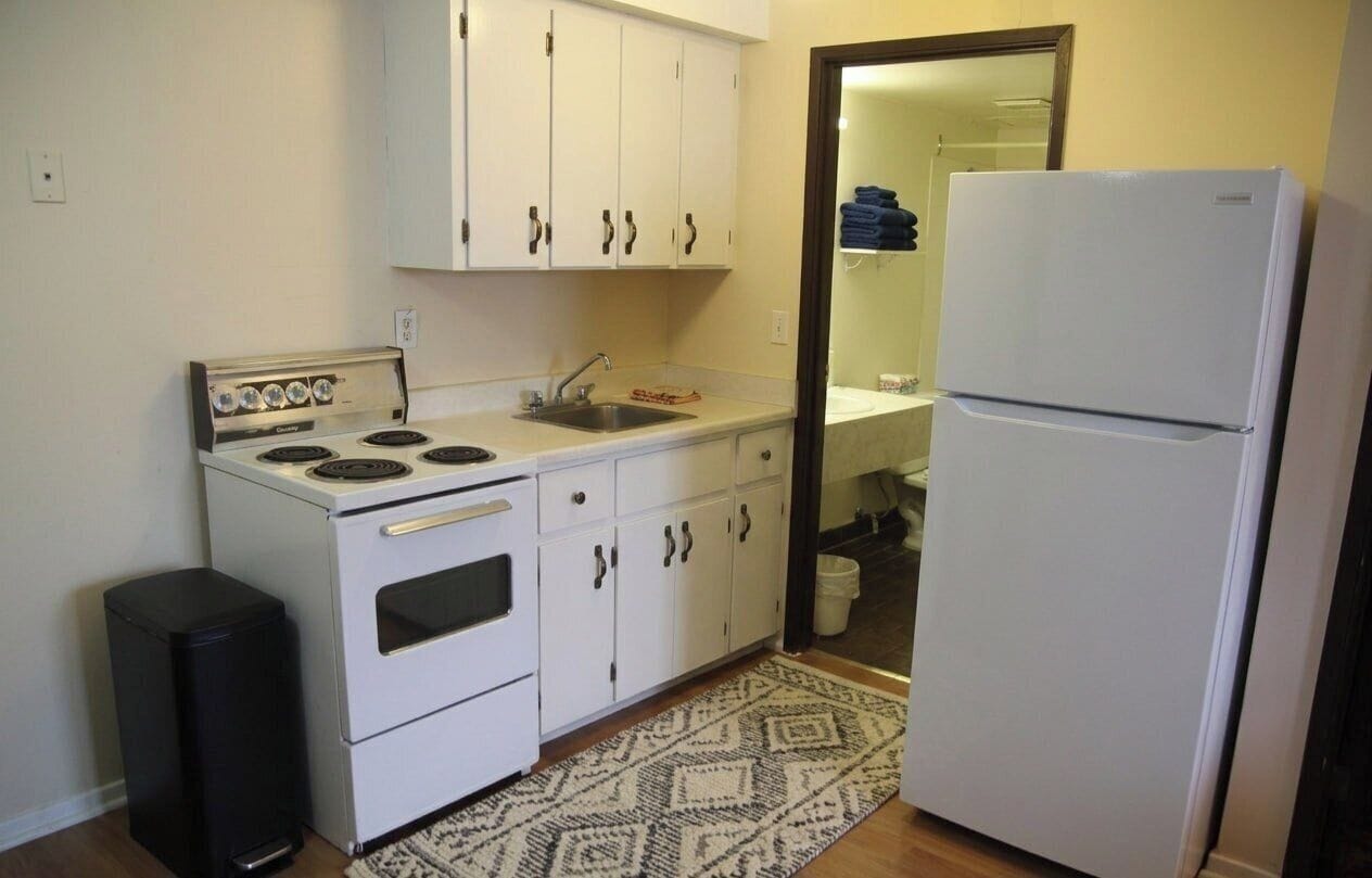 Una cocina funcional con gabinetes blancos, estufa, pileta y refrigerador.
