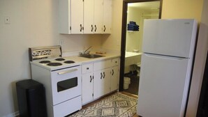 A compact kitchen with white cabinets, a stove, a sink, and a refrigerator. - Shannon Motel (Fort Nelson)