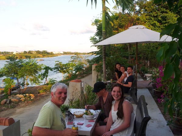 A dining area with a table set for four people, overlooking a body of water. - Homeland River Homestay (Da Nang)