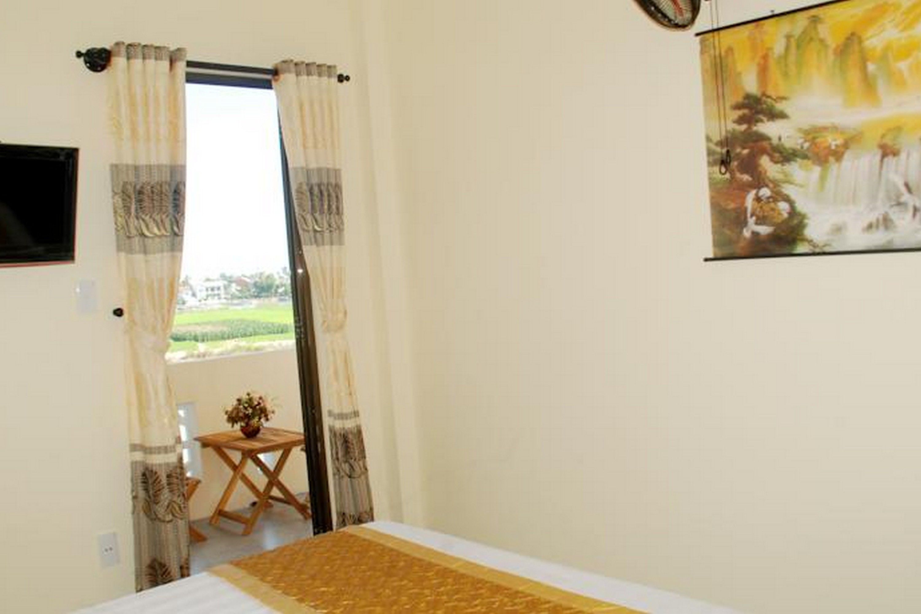 A bedroom with a bed, a small table with a vase, and a painting on the wall.