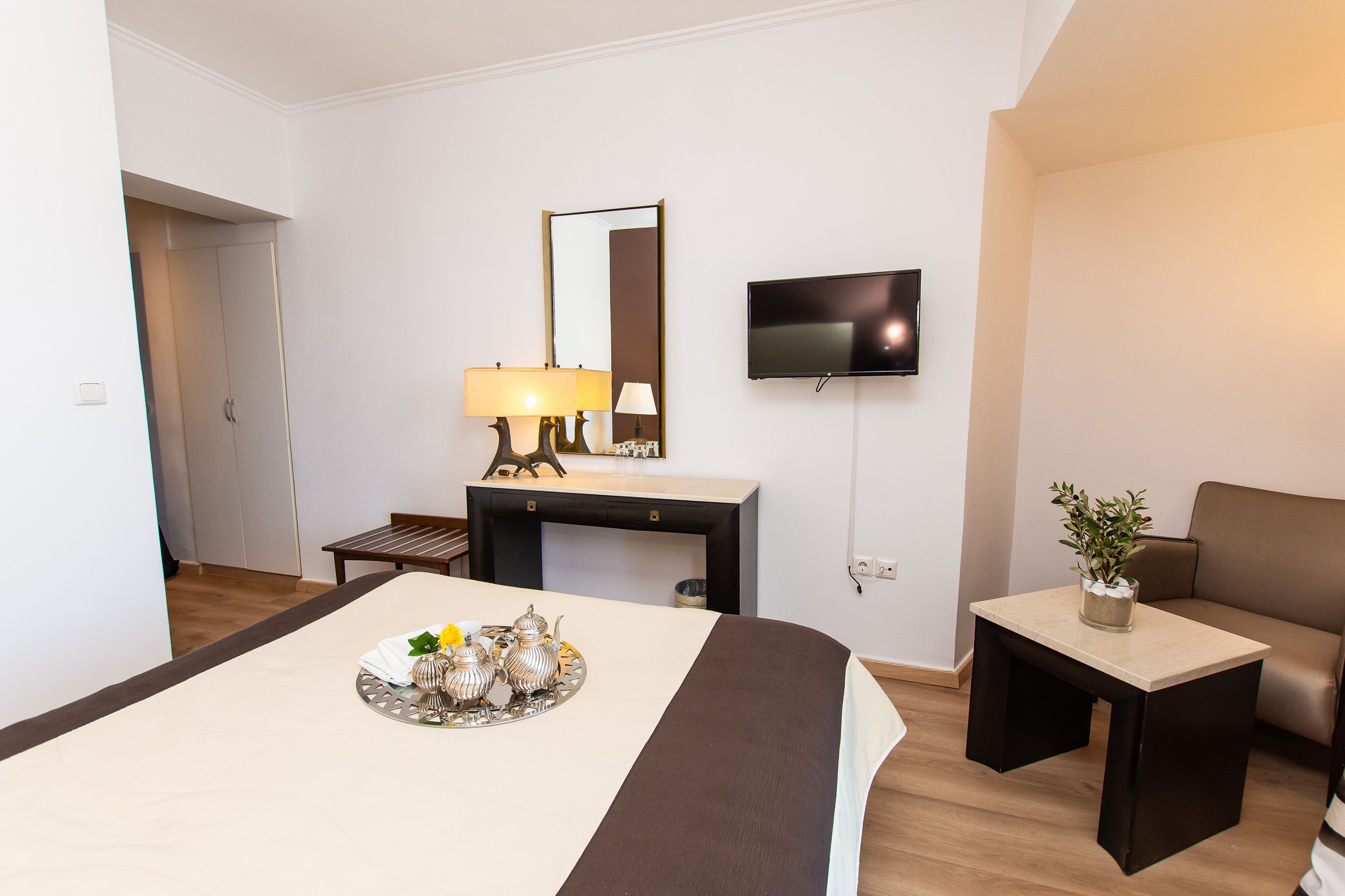 Une chambre d’hôtel avec un lit, un bureau, une télévision et une petite table sur laquelle est posée une plante.