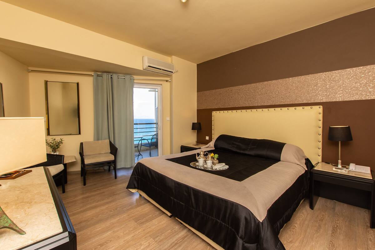 Ein Hotelzimmer mit einem großen Bett, einem Schreibtisch, einem Stuhl, einem Balkon und einer Klimaanlage.