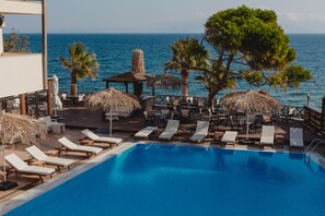 A poolside area with lounge chairs, a thatched-roof structure, and a view of the sea.