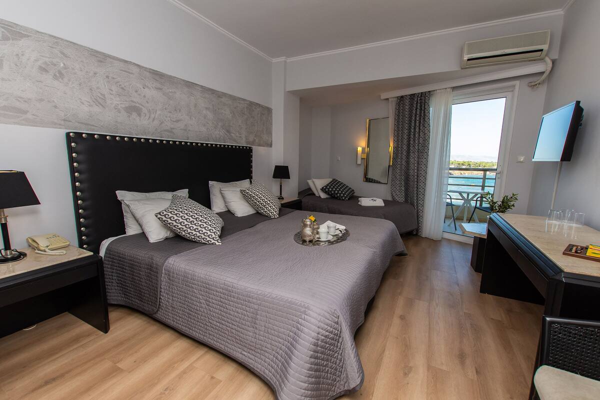 Ein Hotelzimmer mit einem großen Bett, einem Nachttisch mit Lampe, einem Schreibtisch mit Stuhl, einem Flachbildfernseher und einem Balkon mit Blick.