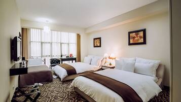 A hotel room with two beds, a desk, a chair, a TV, and artwork on the walls.