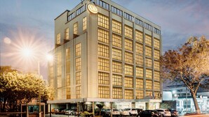 Een meerlaags hotel met een modern ontwerp, met een opvallend bord op de gevel en een parkeerplaats ervoor.
